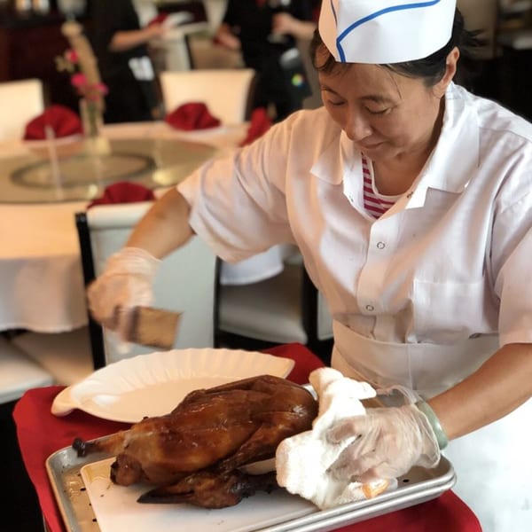 Chef in white uniform and gloves preparing a whole roasted duck on a tray at Mainland China Bistro.