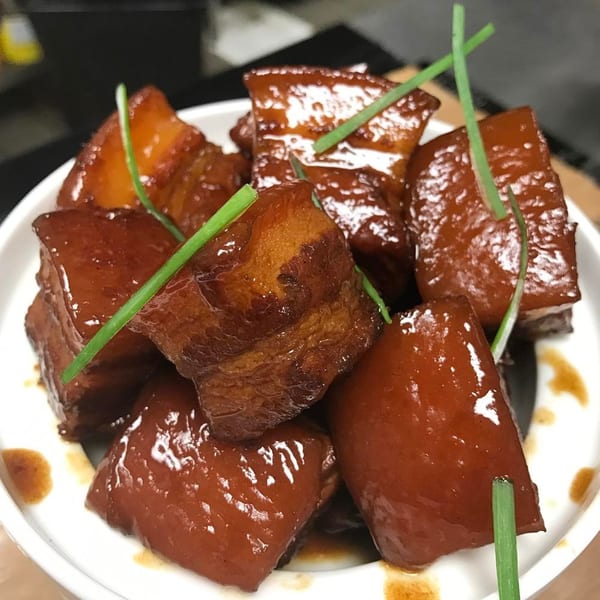 Braised pork belly cubes with a glossy brown sauce and green chives in a white bowl.