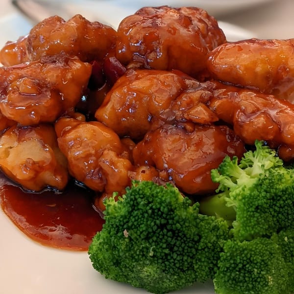 Close-up of Mainland China Bistro's General Tso's chicken with broccoli florets on a white plate.