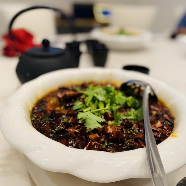 A white bowl of dark Chinese dish with green cilantro and a serving spoon.