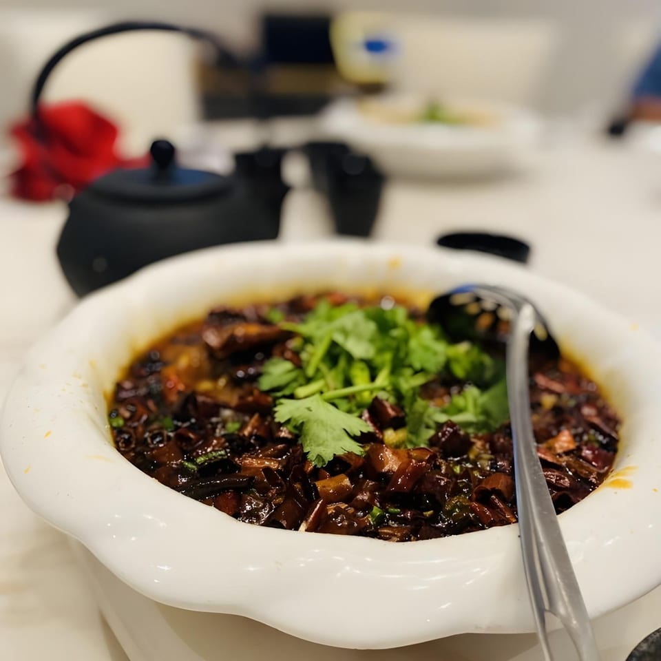 A white bowl of dark Chinese dish with green cilantro and a serving spoon.