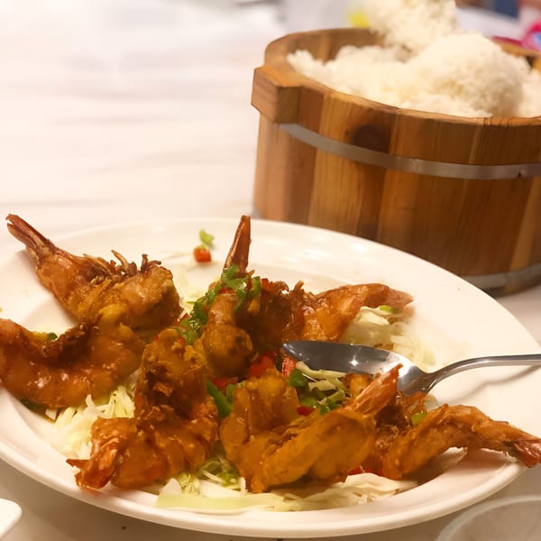 Crispy fried prawns with chili and bell peppers on a bed of shredded cabbage, with a wooden rice bucket.